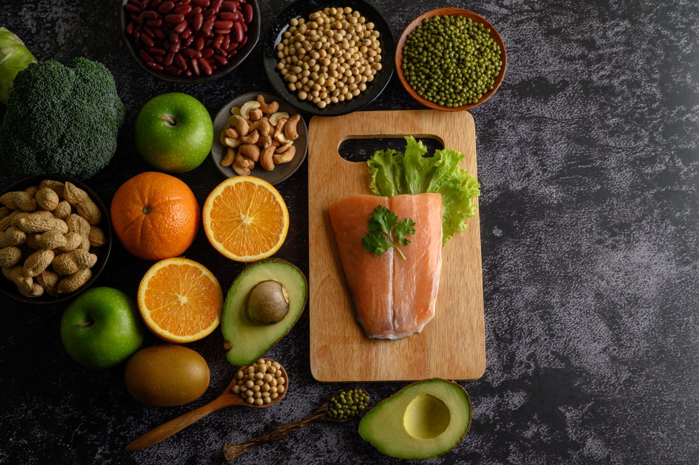 Fresh salmon fillet on a wooden cutting board surrounded by healthy foods like avocado, oranges, apples, broccoli, nuts, and beans, representing brain-boosting foods.