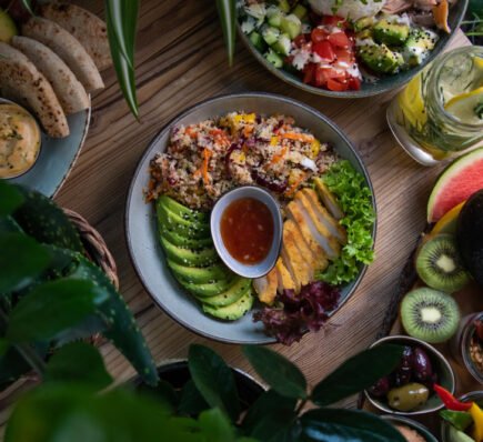 Colorful keto-friendly meal with avocado, chicken, quinoa, salad, and fresh fruits on a wooden table.