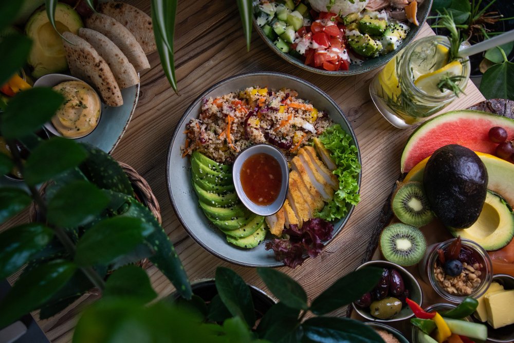 Colorful keto-friendly meal with avocado, chicken, quinoa, salad, and fresh fruits on a wooden table.