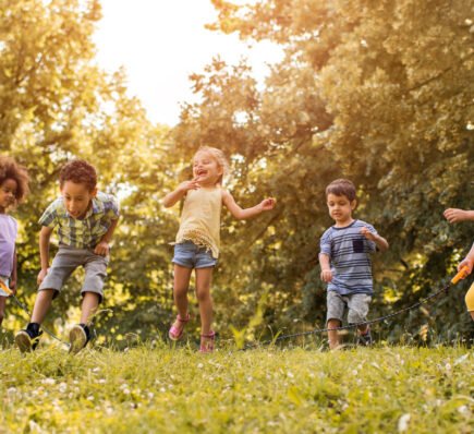Group of happy children playing jump rope together outdoors in a sunny park.