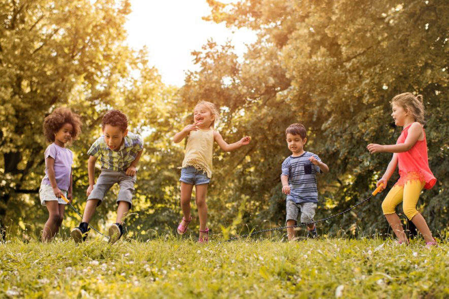 Group of happy children playing jump rope together outdoors in a sunny park.