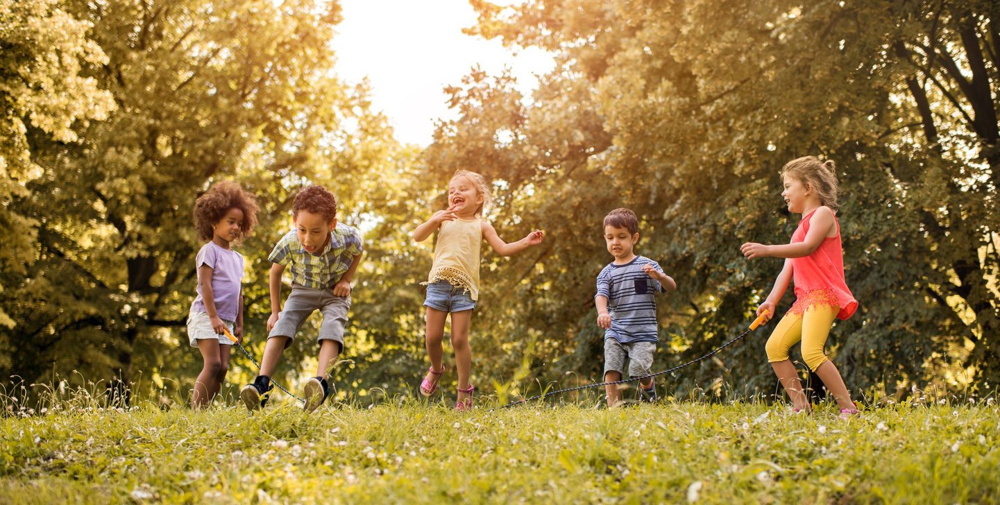 Group of happy children playing jump rope together outdoors in a sunny park.